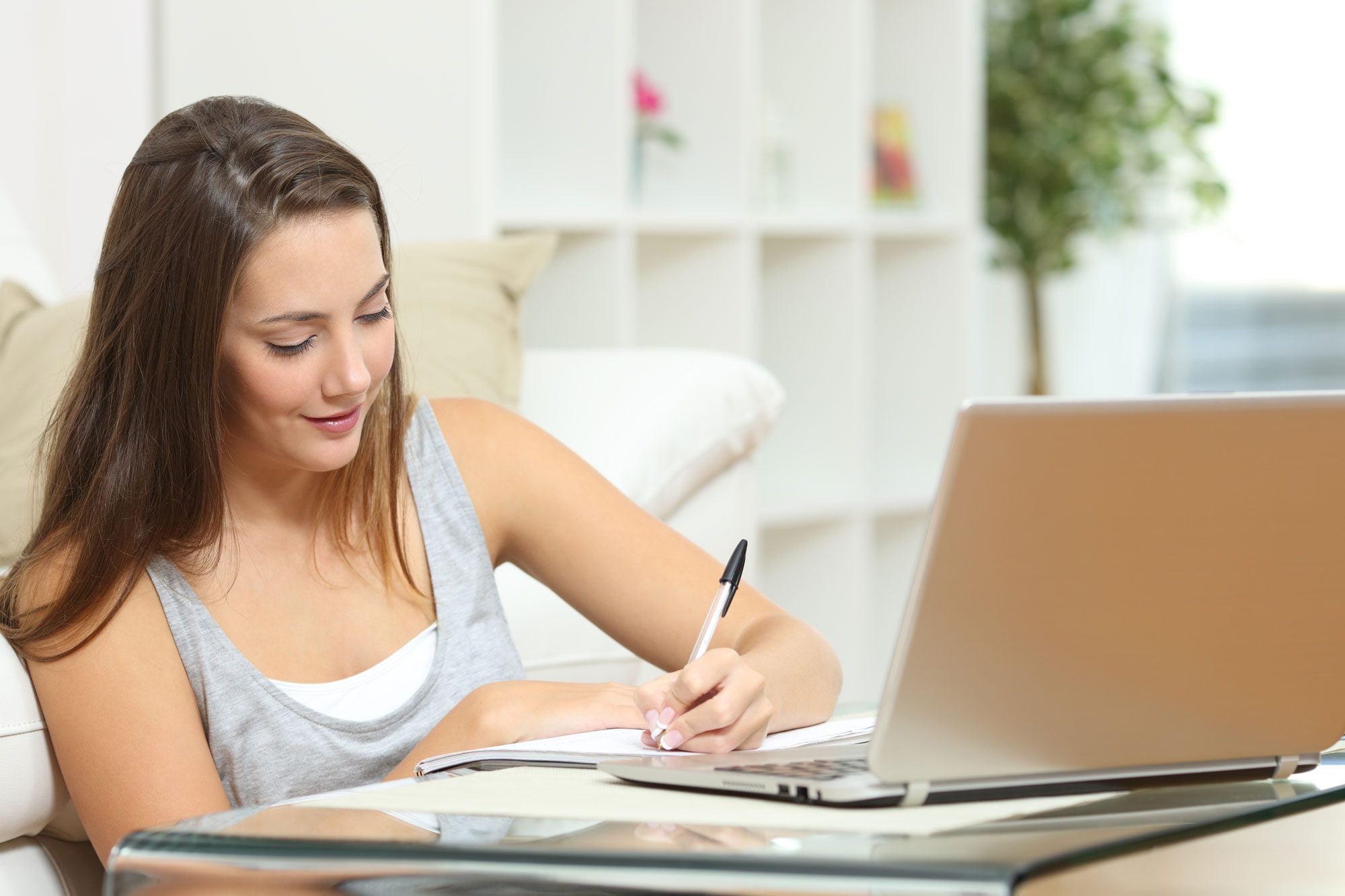 Adult writing in a notebook next to an open laptop.